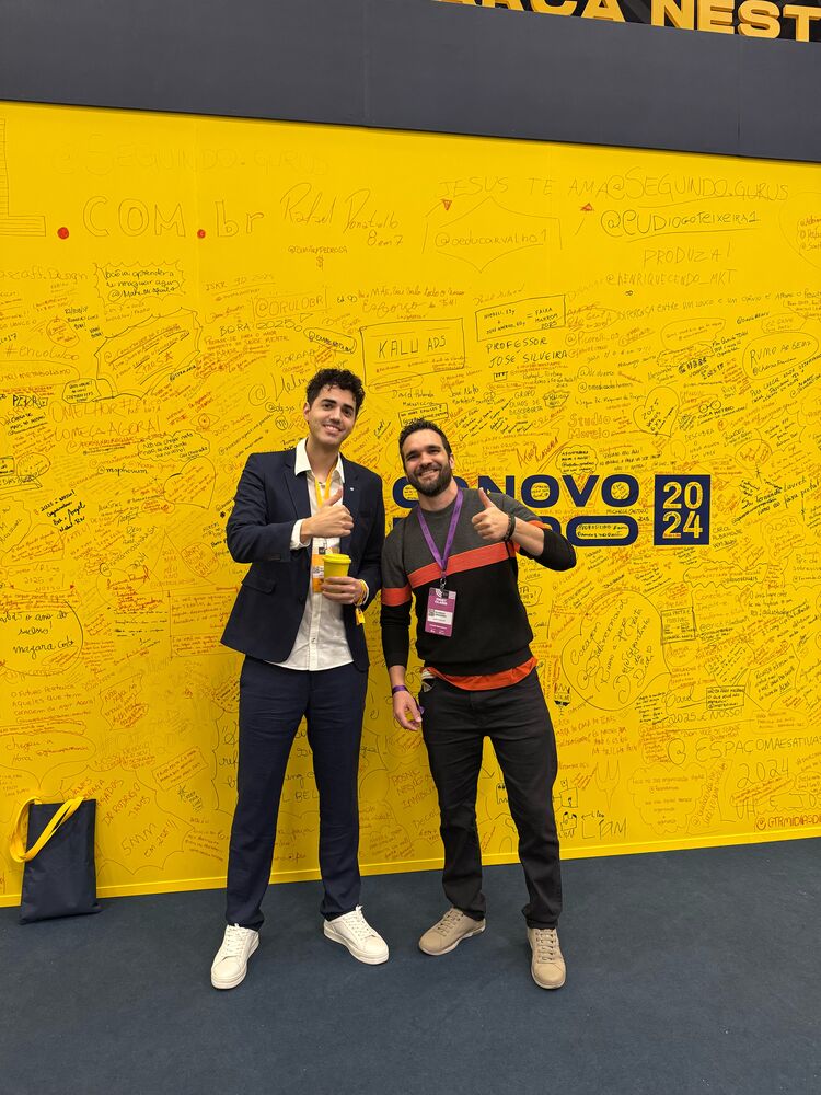 Ricardo e outro participante diante do painel amarelo do O Novo Mundo 2024